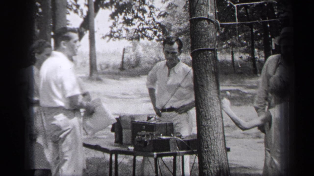 Adults standing outdoors near a small table with a portable record player under trees.