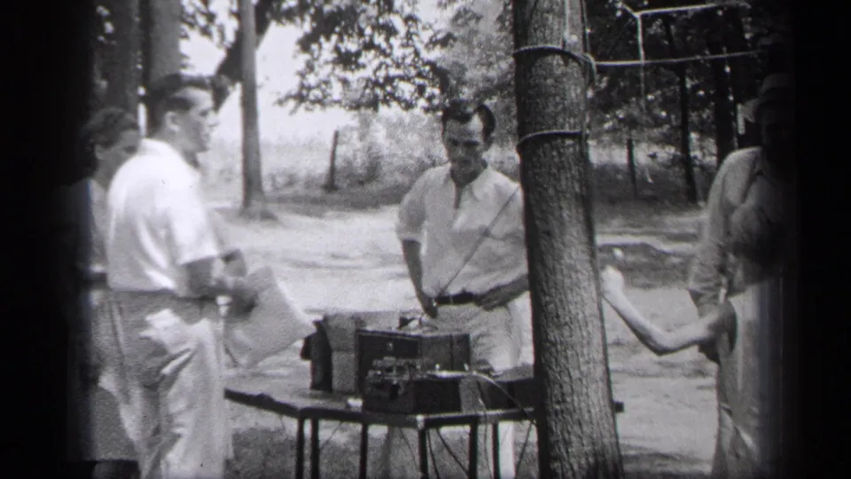 1937 Cleveland 8mm frame showing adults gathered in a wooded outdoor area around a tabletop record player.