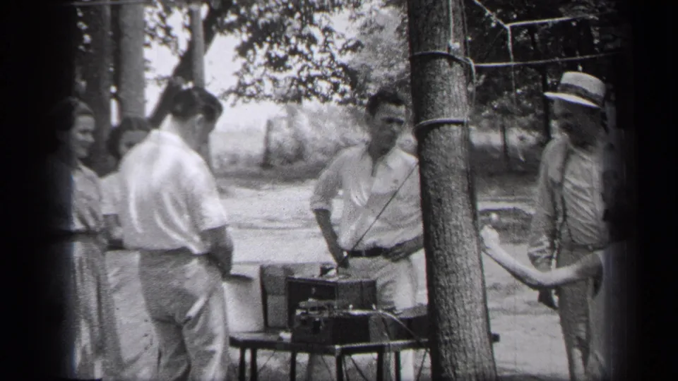 Adults in period clothing gather around a small outdoor table with record player equipment in Cleveland, 1937.