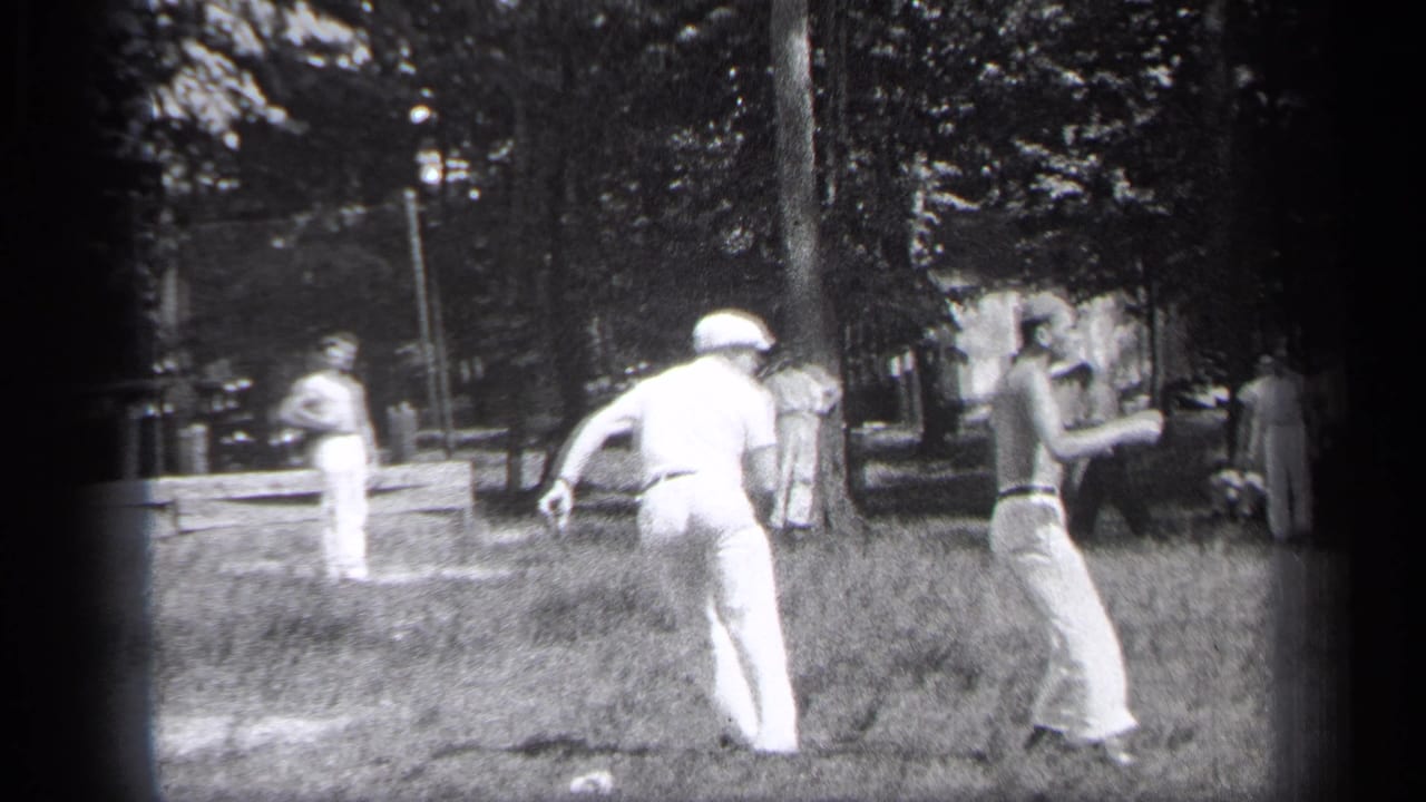 A man in white runs across a grassy baseball field toward another man near trees.