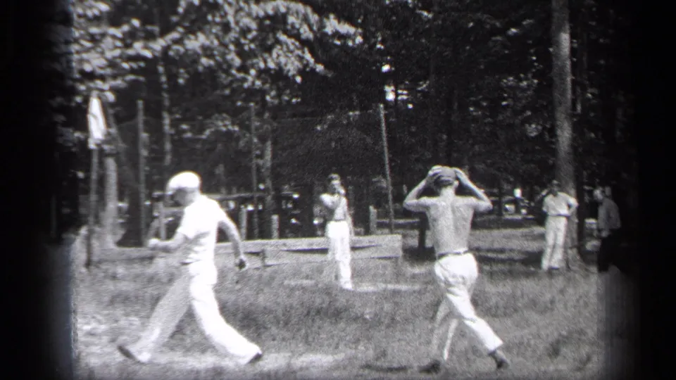 Cleveland 1937 home-movie frame of men during a casual park baseball game, including a shirtless player and onlookers.