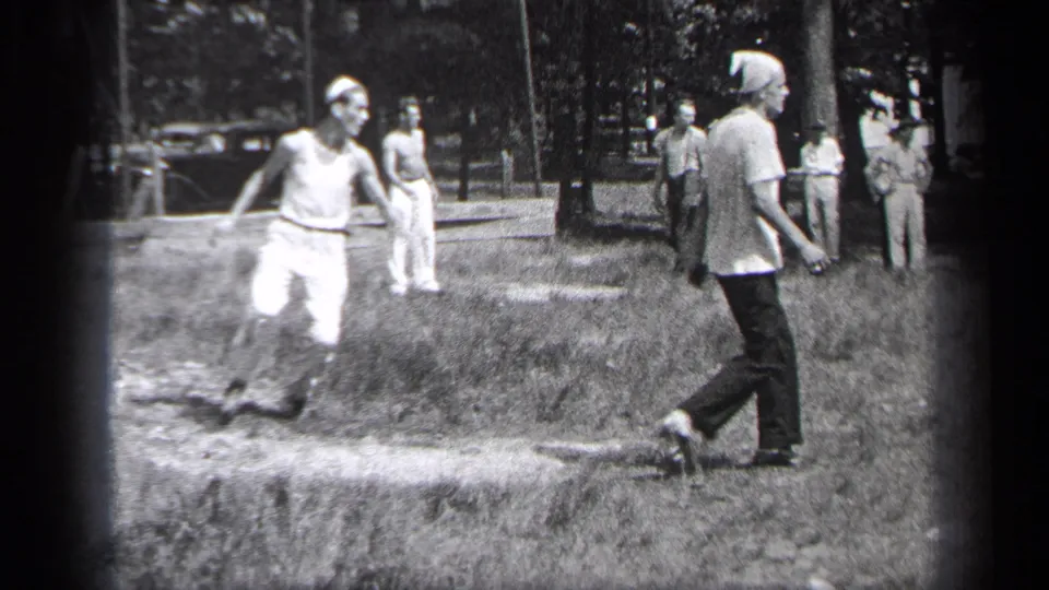 1937 Cleveland park baseball frame showing a runner, a capped onlooker, trees, and several men watching from the field edge.