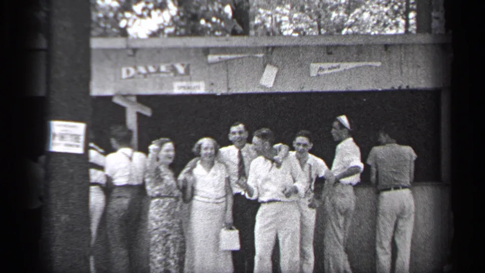 In 1937 Cleveland home-movie footage, adults in dresses, shirts, and ties gather near a DAVEY-marked outdoor venue.