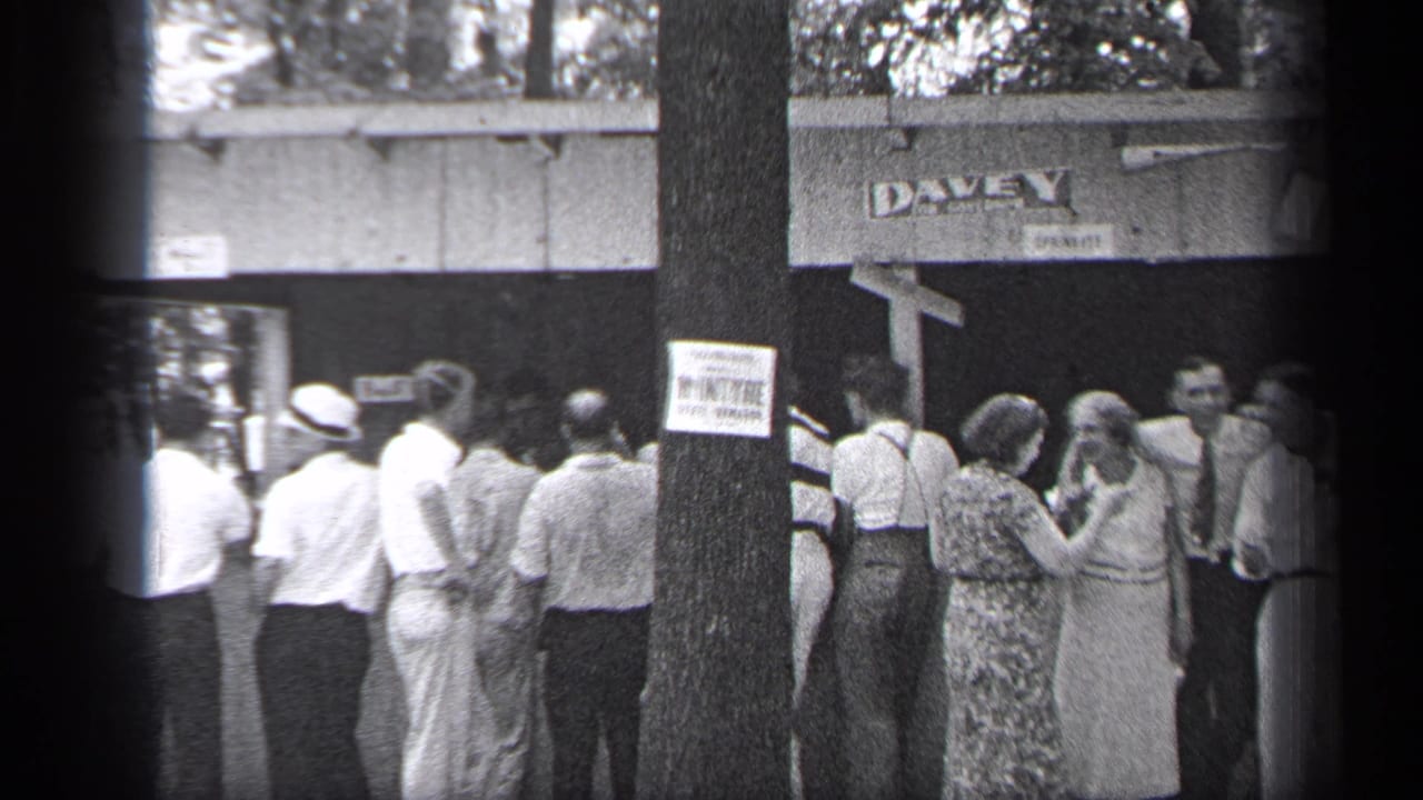 Adults stand in a line outside a building marked DAVEY, with a posted sign on a tree in front.