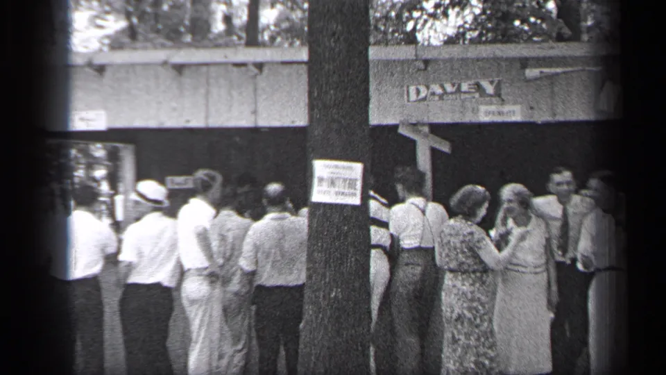 In 1937 Cleveland, adults in hats, shirts, and dresses wait outside a building marked DAVEY, partly blocked by a tree with a sign.