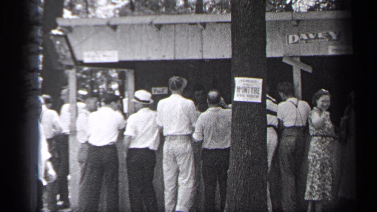 A crowd of adults faces a booth or entrance, with a DAVEY sign above and a sign posted on a tree.