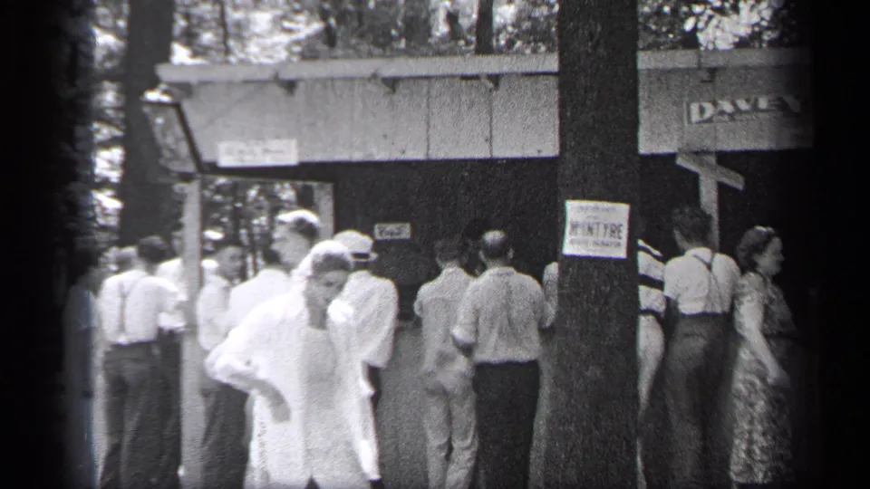 A Cleveland 1937 home-movie frame shows adults waiting near the DAVEY-marked building as a person in light clothing passes close to camera.