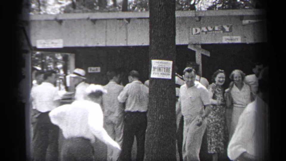 1937 Cleveland home-movie frame showing a sidewalk crowd near a tree, posted notice, and DAVEY sign, with men and women gathered outdoors.