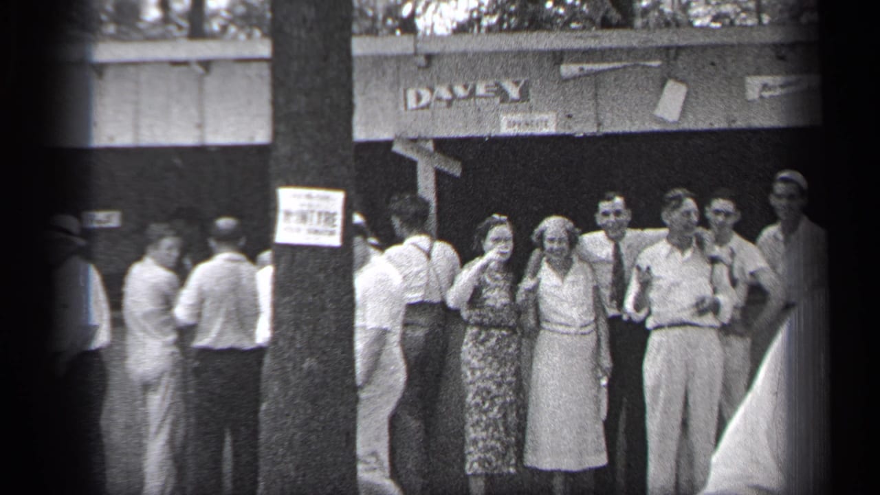 Group of adults standing near a building sign while pedestrians move through the sidewalk scene.
