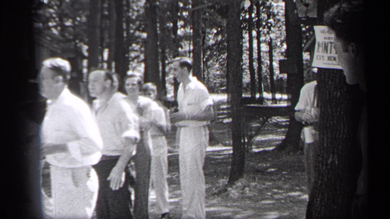 Men in light clothing stand among trees near a posted sign in a park.