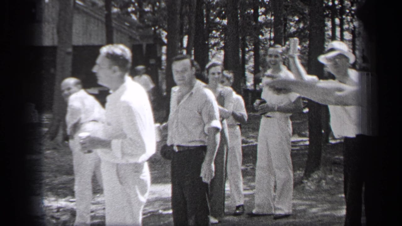 Several men stand near trees, with one man raising a hand at the edge of frame.