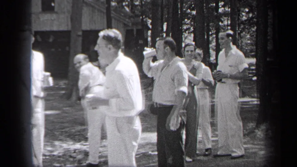 Adult men in 1937 Cleveland stand in a wooded park clearing as one drinks from a bottle during the gathering.