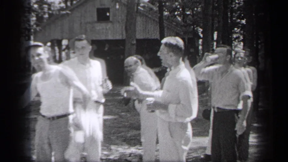 The 1937 Cleveland park gathering continues as men turn, gesture, and hold bottles in soft handheld 8mm footage.