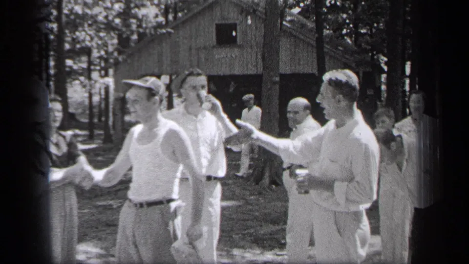 In 1937 Cleveland home-movie footage, men in light summer clothing greet each other outdoors near trees and a rustic structure.