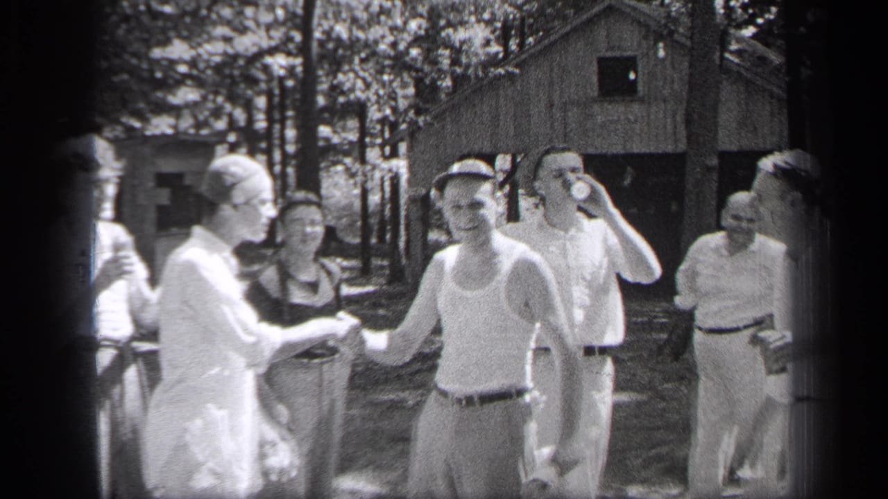 A man in a cap shakes hands while another man drinks from a can behind him.