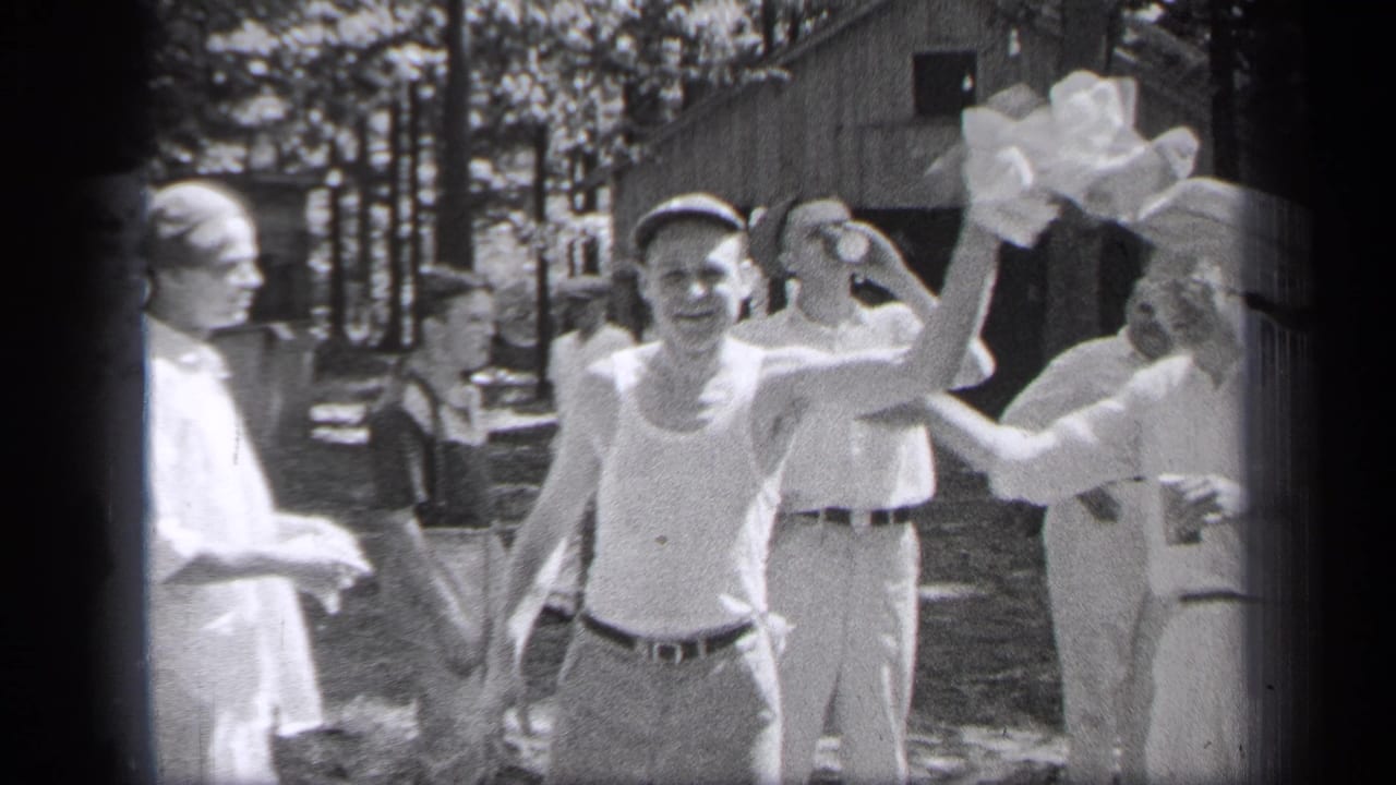 1937 Cleveland home-movie frame showing adults outdoors near a cabin, with one man in a tank top facing the camera.
