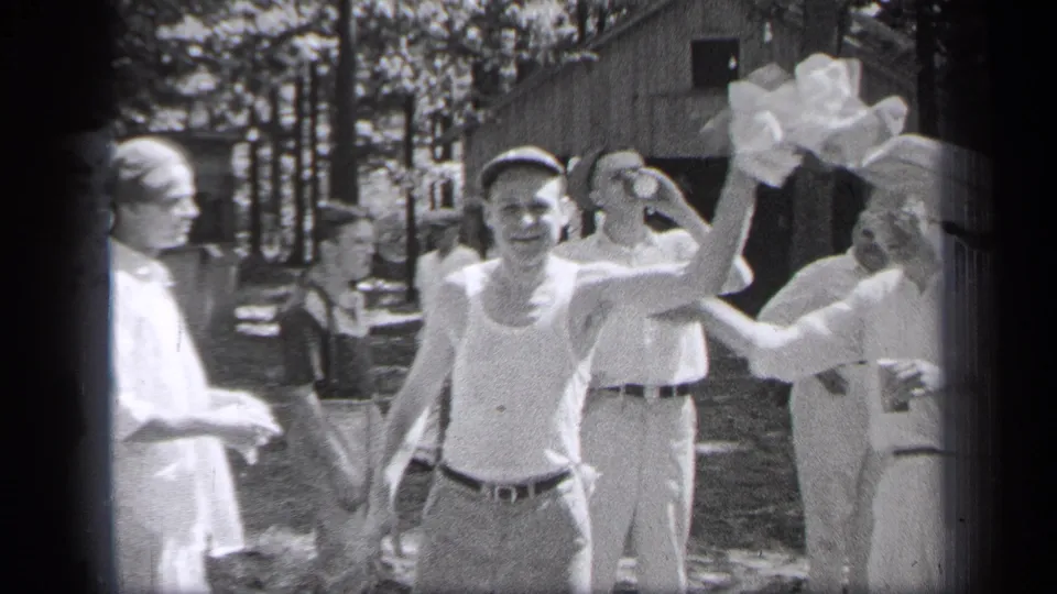 1937 Cleveland home-movie frame showing adults outdoors near a cabin, with one man in a tank top facing the camera.