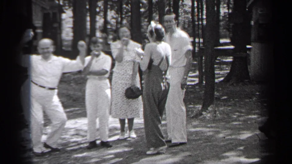 1937 Cleveland home-movie frame showing adults posing and talking near trees, with a man leaning at the left.