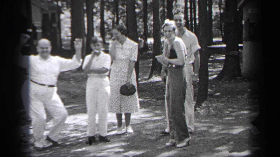 1937 Cleveland home-movie frame of adults in summer clothing gathered near trees, with a woman turned toward the camera.
