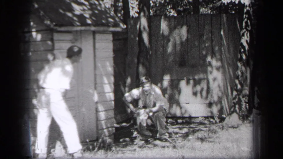 In 1937 Cleveland home-movie footage, two adult men are near a small wooden shed as one crouches by an object in the yard.