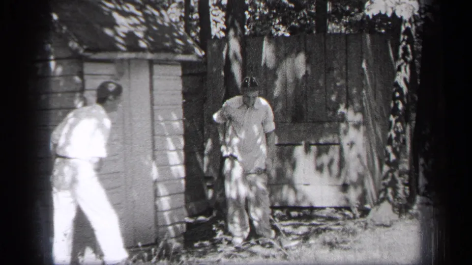 The 1937 Cleveland home movie shows two men standing close to a wooden shed in a shaded backyard area.