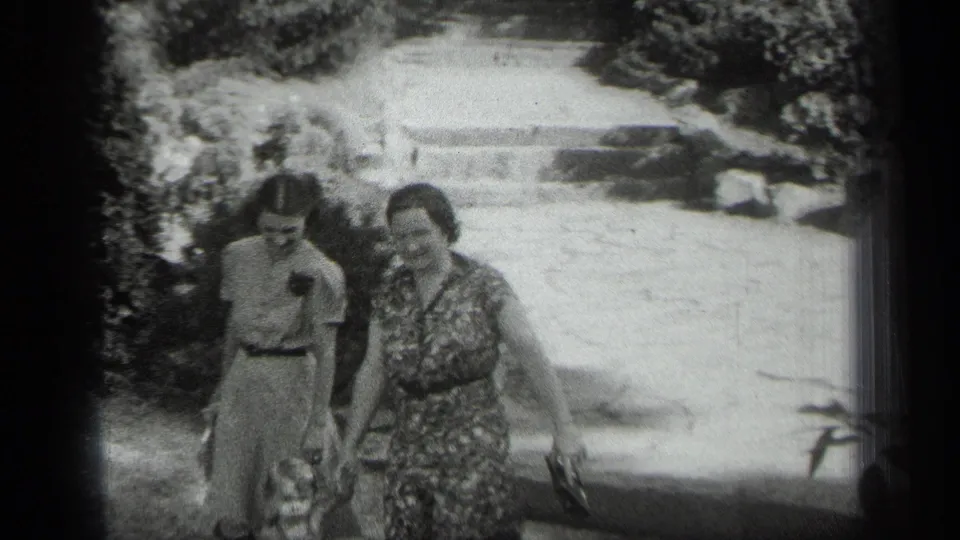 The two women are closer to the camera, walking along the garden path in black-and-white 8mm footage from Cleveland.