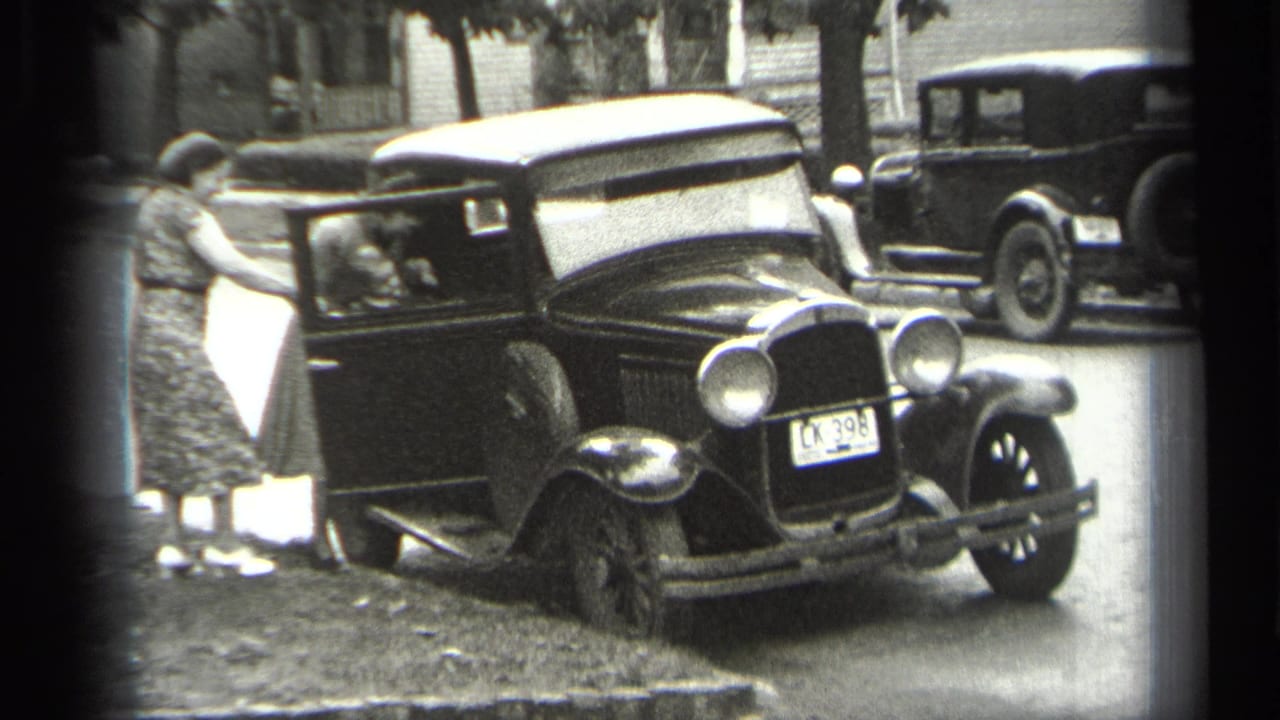 Woman beside an open door of a black sedan as another person sits inside.