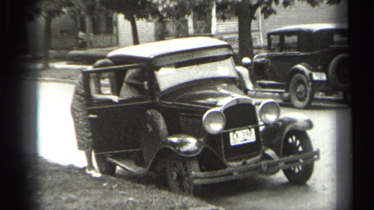 Black sedan with its driver-side door open and an adult partly visible at the doorway.