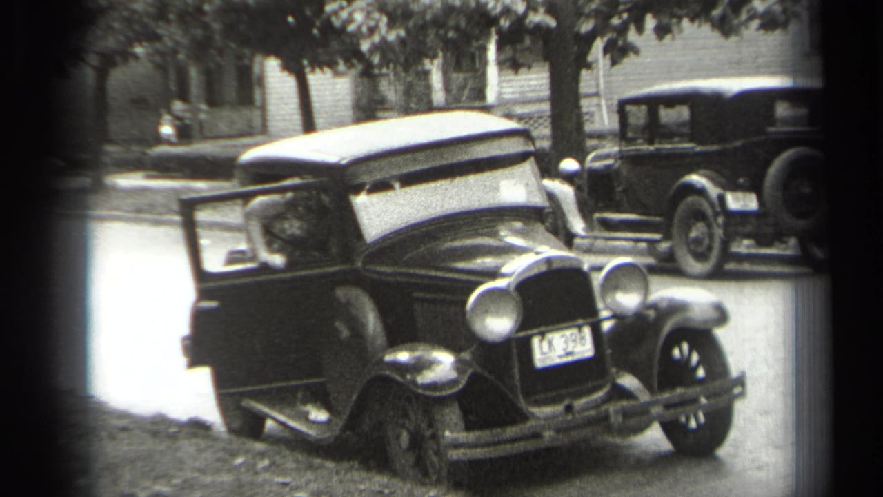 Dark 1930s sedan with open driver-side door on a residential street.