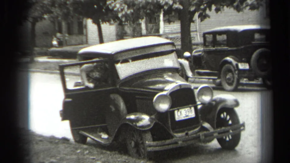 Cleveland 1938 home-movie frame showing a dark sedan with a light roof, open door, seated driver, and another parked car nearby.