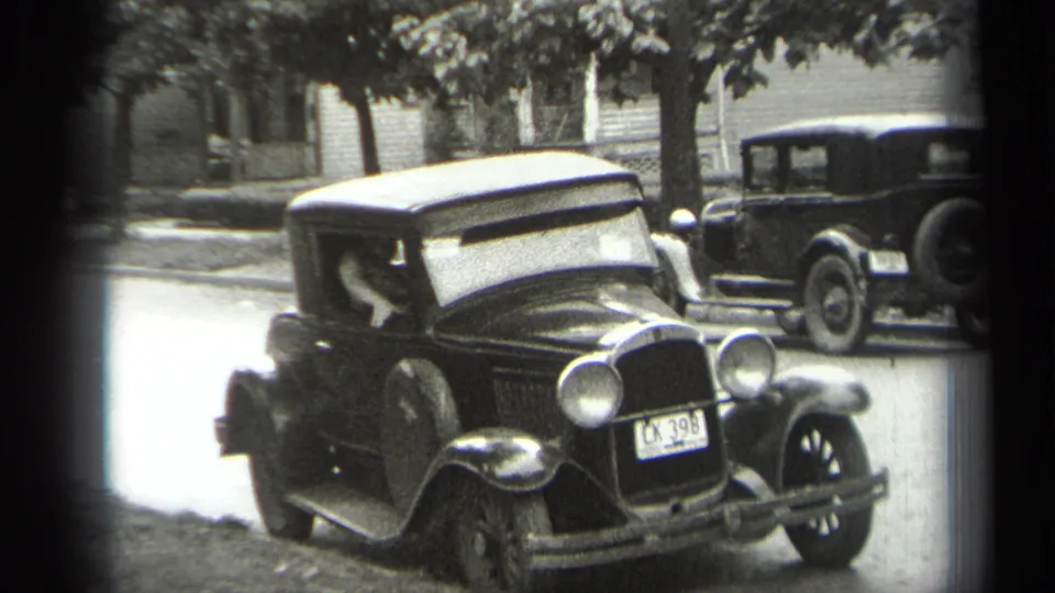 Cleveland 1938 frame showing a dark 1930s sedan, driver at the open door, front fender and plate visible on a residential street.