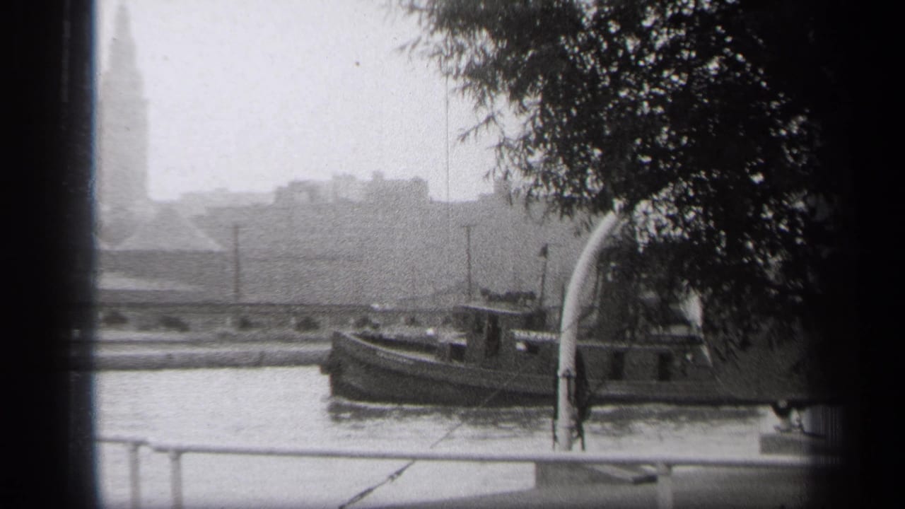 Tugboat moving past a riverside railing with trees overhead.