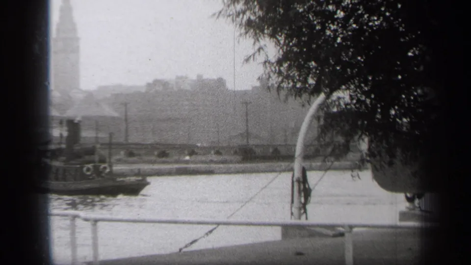At the end of the 1938 Cleveland view, the tugboat is mostly off left while the river, railing, tree canopy, and distant tower remain visible.