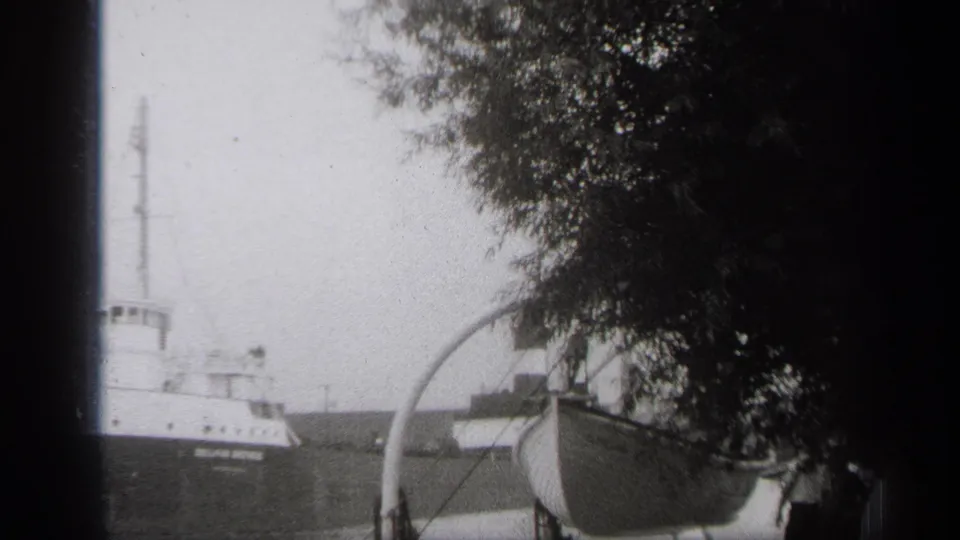 Cleveland waterfront view of a cargo vessel moving past a small foreground boat under heavy tree cover.