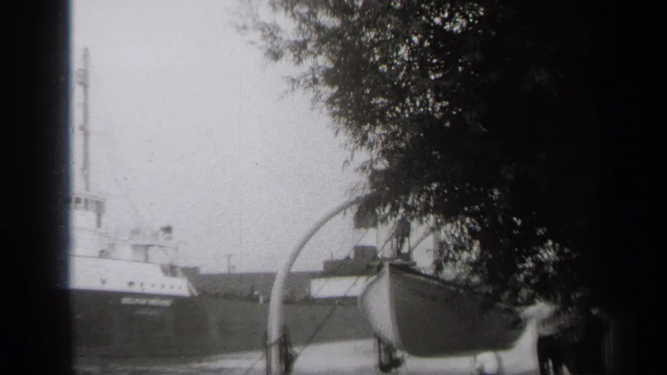 1938 Cleveland shoreline frame with a cargo ship, a boat on a trailer, trees, and a small person partly visible at the right.