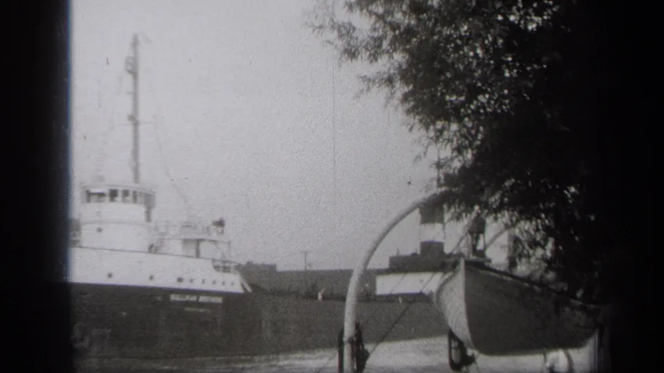 1938 Cleveland harbor view of the SULLIVAN BROTHERS freighter moving past a small foreground boat and trees.