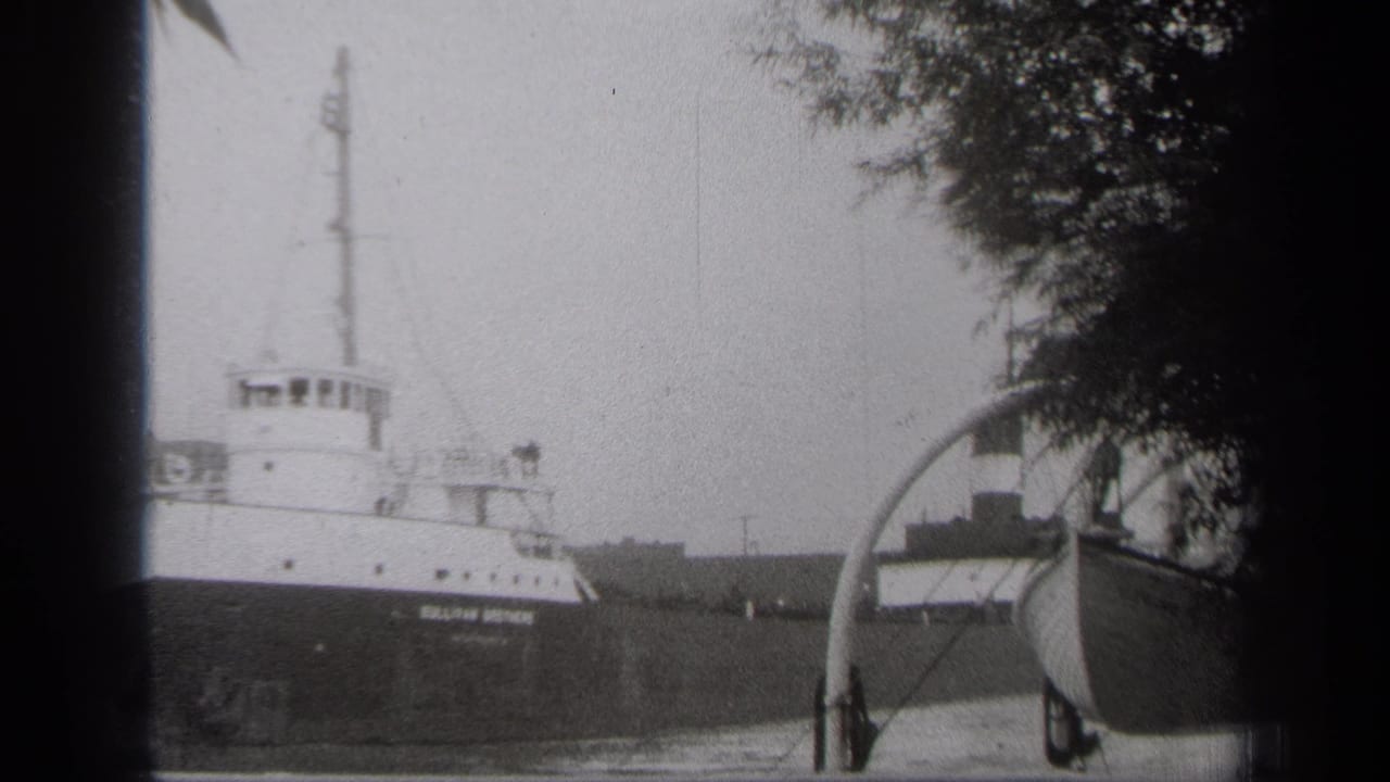 Large freighter with visible hull lettering moving past a small boat near shore.