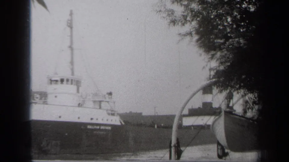 The SULLIVAN BROTHERS freighter moves through the Cleveland waterway, partly framed by a small boat and tree cover.