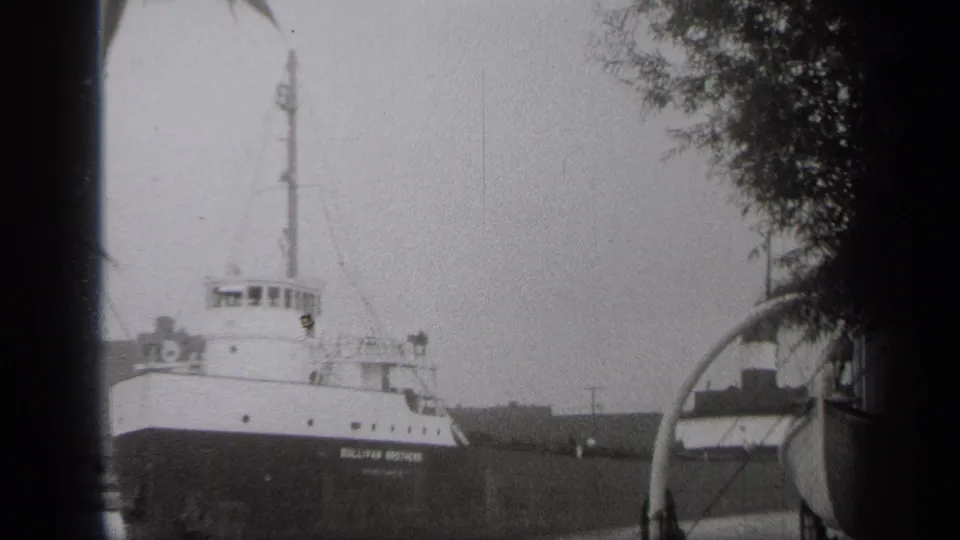 A close shoreline view shows the freighter bow and superstructure in the 1938 Cleveland industrial waterway scene.