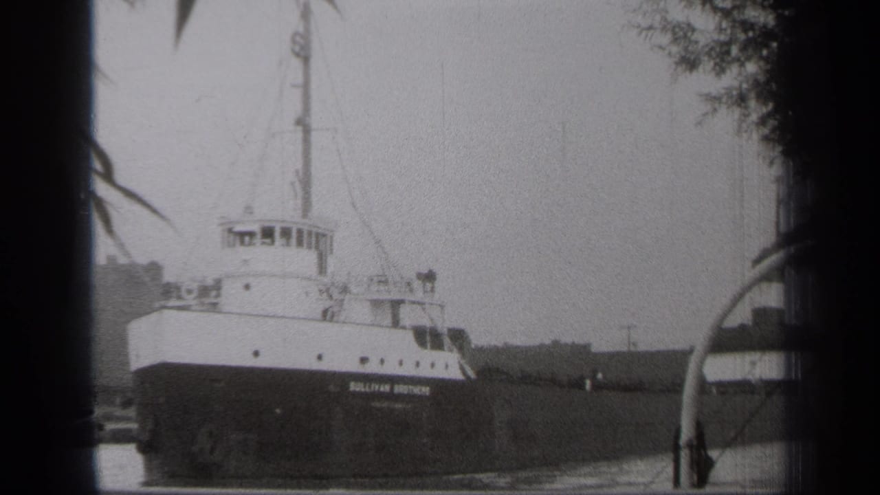 1938 Cleveland home-movie frame showing the Sullivan Brothers vessel stationary in calm water, partly framed by dark leaves.