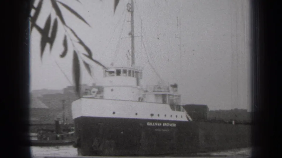 A closer 1938 Cleveland frame shows the docked Sullivan Brothers vessel, its cabin windows, dark hull, and foreground branches.
