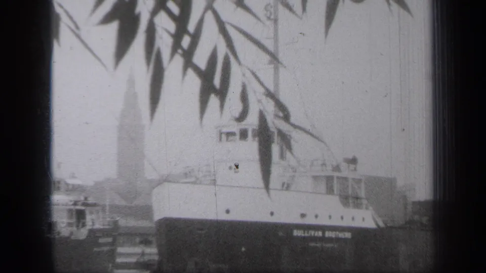 1938 Cleveland waterfront frame showing the SULLIVAN BROTHERS ship through foliage, with nearby vessels and shore structures in the background.