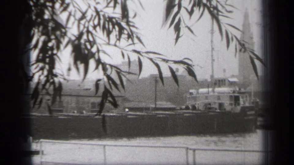 1938 Cleveland river view with a large vessel moving behind silhouetted branches and a low riverside railing.