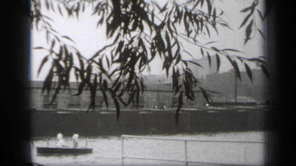 Two men appear on a small boat near the Cleveland riverfront while a larger vessel moves in the background.