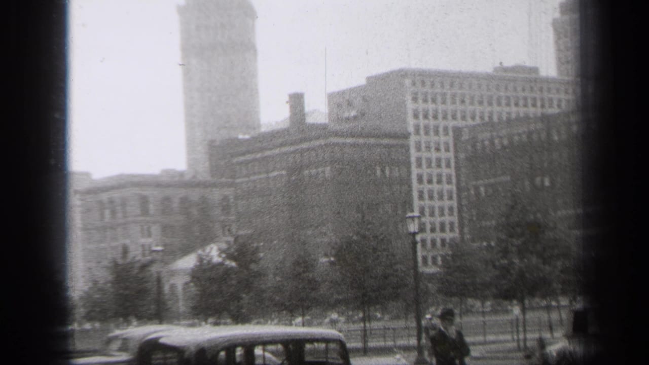 Hazy downtown street with parked cars, trees, buildings, and a tall tower in the background.