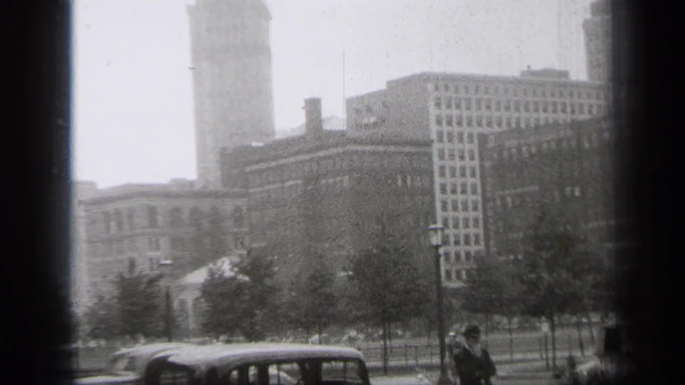 1938 Cleveland street view with parked period cars, trees, lampposts, downtown buildings, and a tall tower seen through haze.
