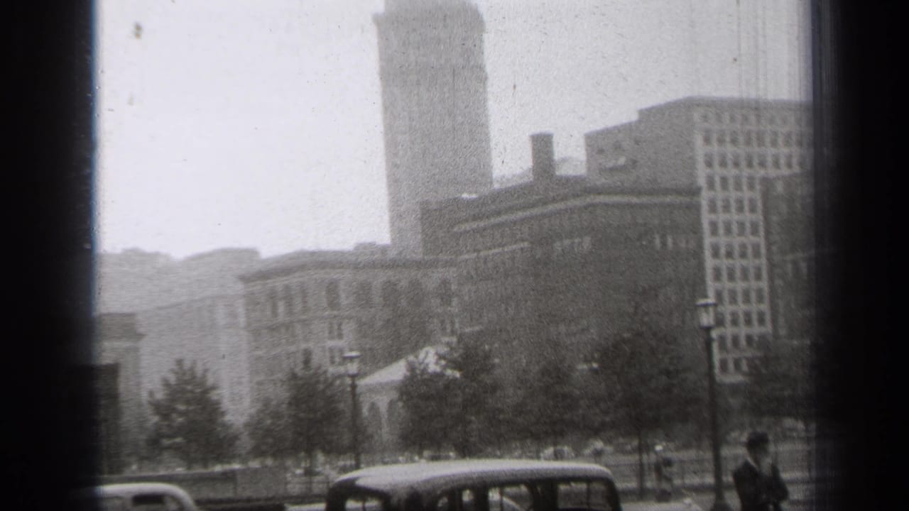 Downtown buildings and trees with parked cars and a man partly visible at the sidewalk edge.