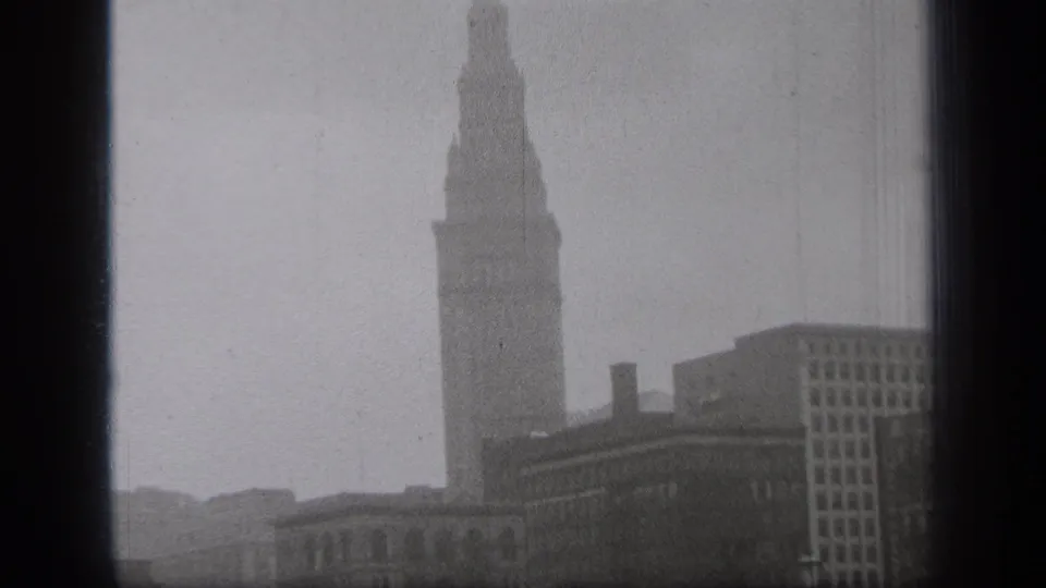 Soft-focus Cleveland tower view from 1938 with fog, lower downtown buildings, and visible 8mm frame borders.