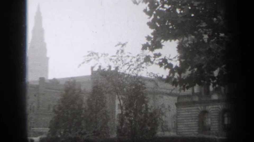 1938 Cleveland footage frame showing a spired tower behind trees, with a dark window edge and grainy black-and-white texture.