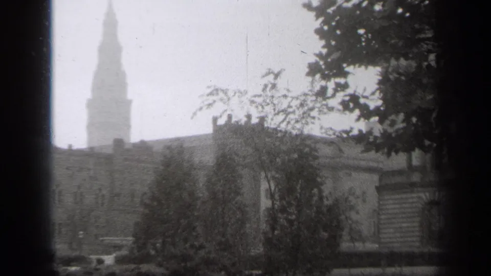 1938 Cleveland black-and-white frame with a tall spire, masonry rooftops, trees, and dark window borders.
